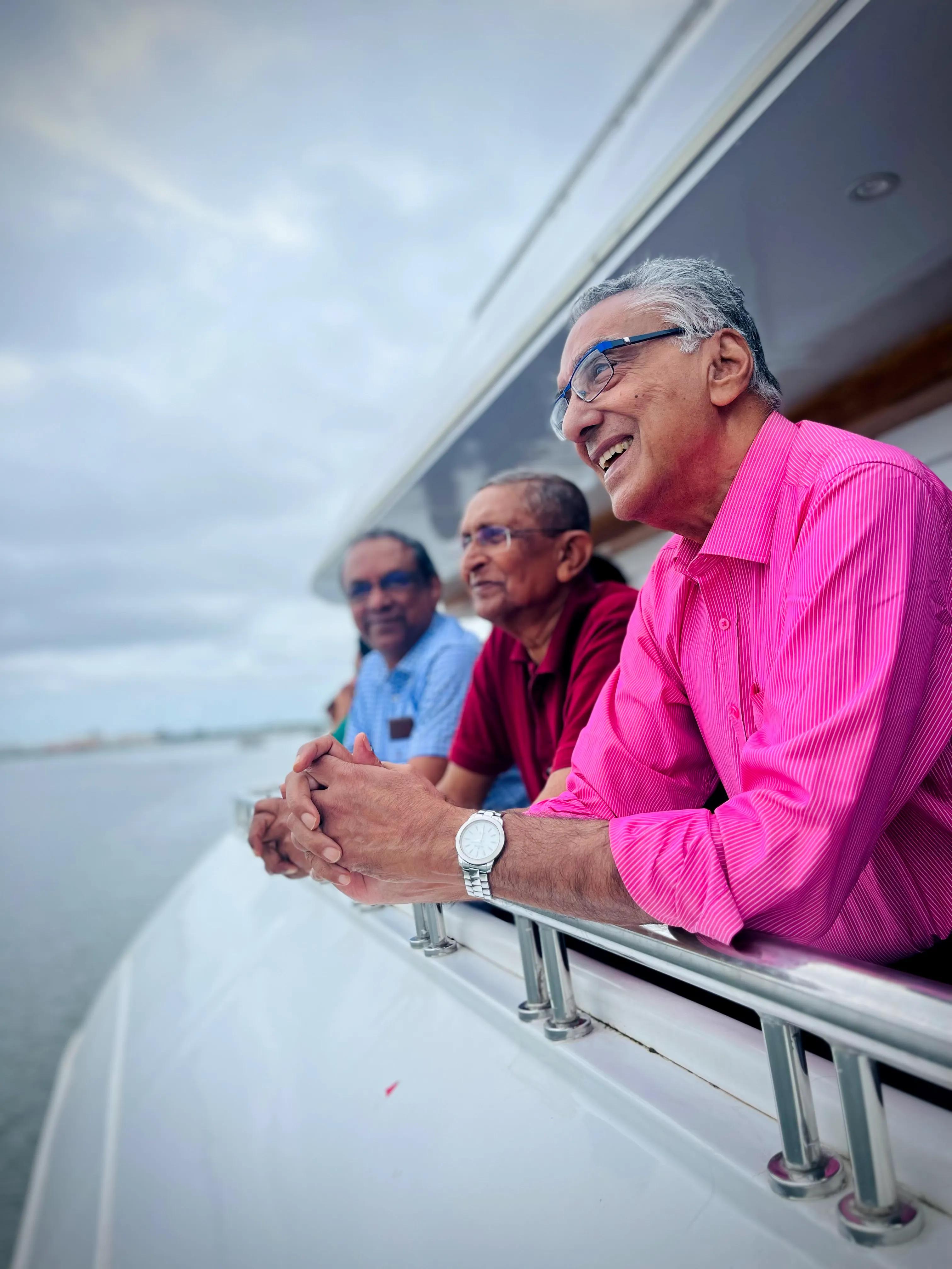  Three senior men enjoying a scenic cruise aboard Minar Cruise, gazing out from the deck while sailing along the Arabian Sea