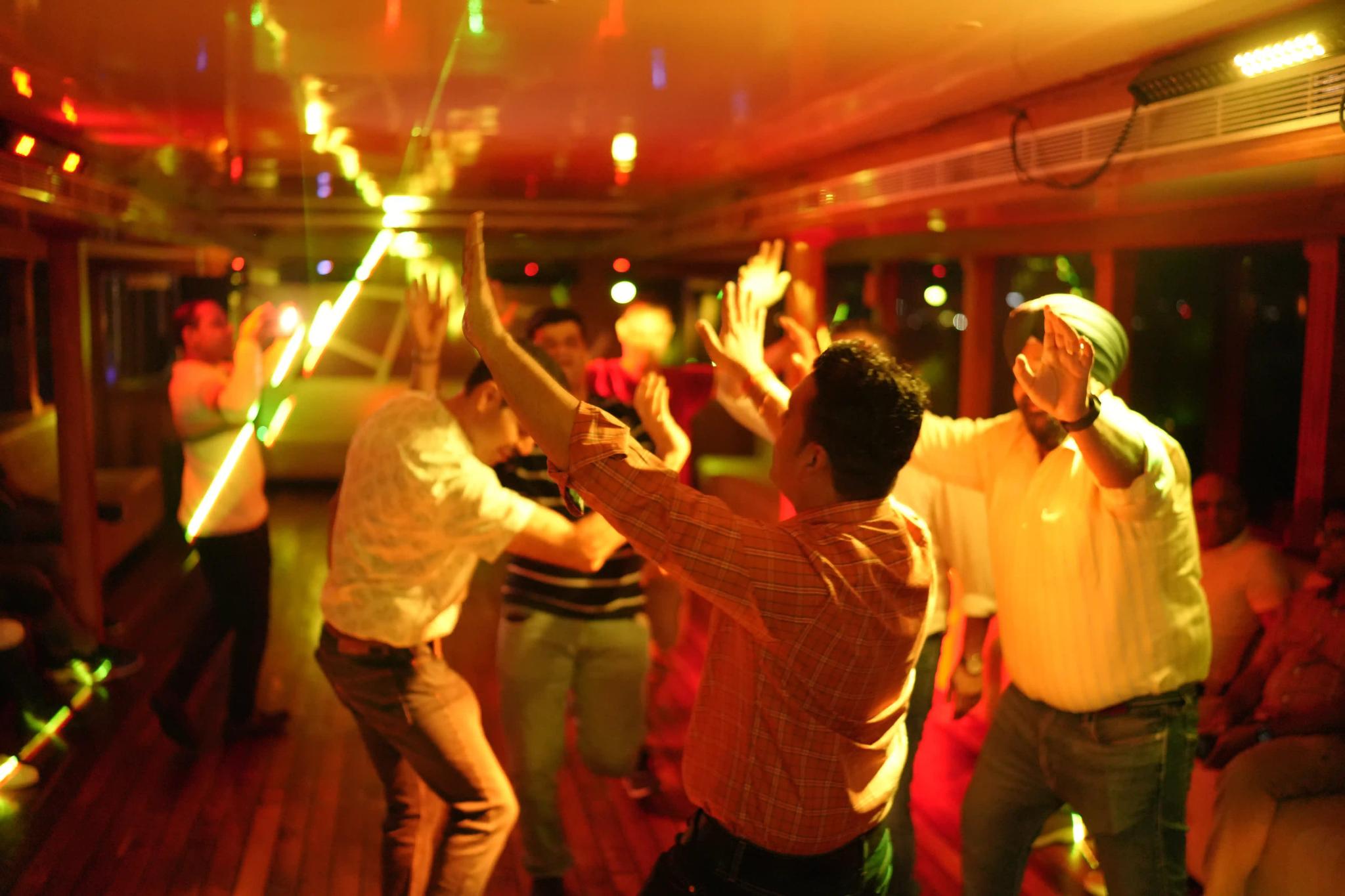 A group of friends dances the night away at a party. The lighting is dim and warm, and the people are all smiling and laughing. It's a great night to let loose and have some fun